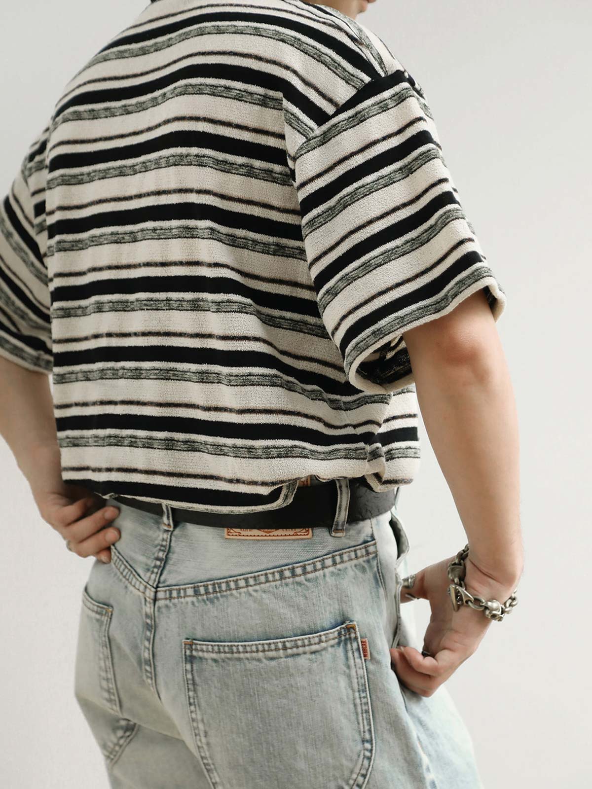 モデルがブラック&ホワイト・ストライプ・ショートスリーブTシャツを着用し、その全体的なスタイルとフィット感を示しています