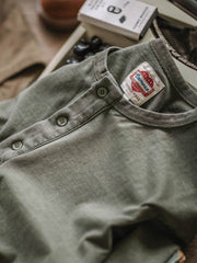 ヘンリーネックTシャツの開襟部分のクローズアップ。ビンテージウォッシュ加工による独特のテクスチャと色合いが見て取れる。