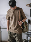 モデルがヘンリーネック半袖Tシャツを着用し、カジュアルパンツとシンプルなキャンバスシューズでコーディネート。リラックスしたが洗練されたカジュアルスタイルを演出している。