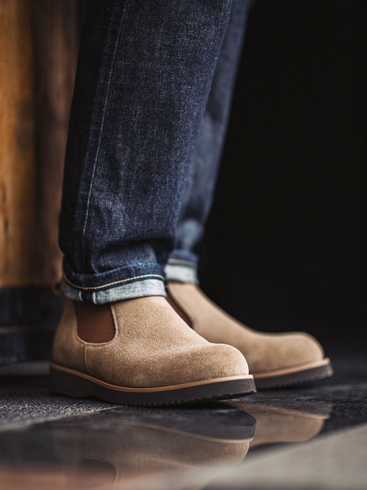 詳細画像:
チェルシーブーツのゴムバンドとスエードの質感がクローズアップされたディテール画像。履きやすさとデザインの美しさが強調されています。
モデル画像:
モデルがライトブラウンスエードチェルシーブーツを履いたスタイル。カジュアルからワークスタイルまで、多様なコーディネートに対応可能なアイテムです。