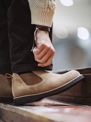 詳細画像:
チェルシーブーツのゴムバンドとスエードの質感がクローズアップされたディテール画像。履きやすさとデザインの美しさが強調されています。
モデル画像:
モデルがライトブラウンスエードチェルシーブーツを履いたスタイル。カジュアルからワークスタイルまで、多様なコーディネートに対応可能なアイテムです。