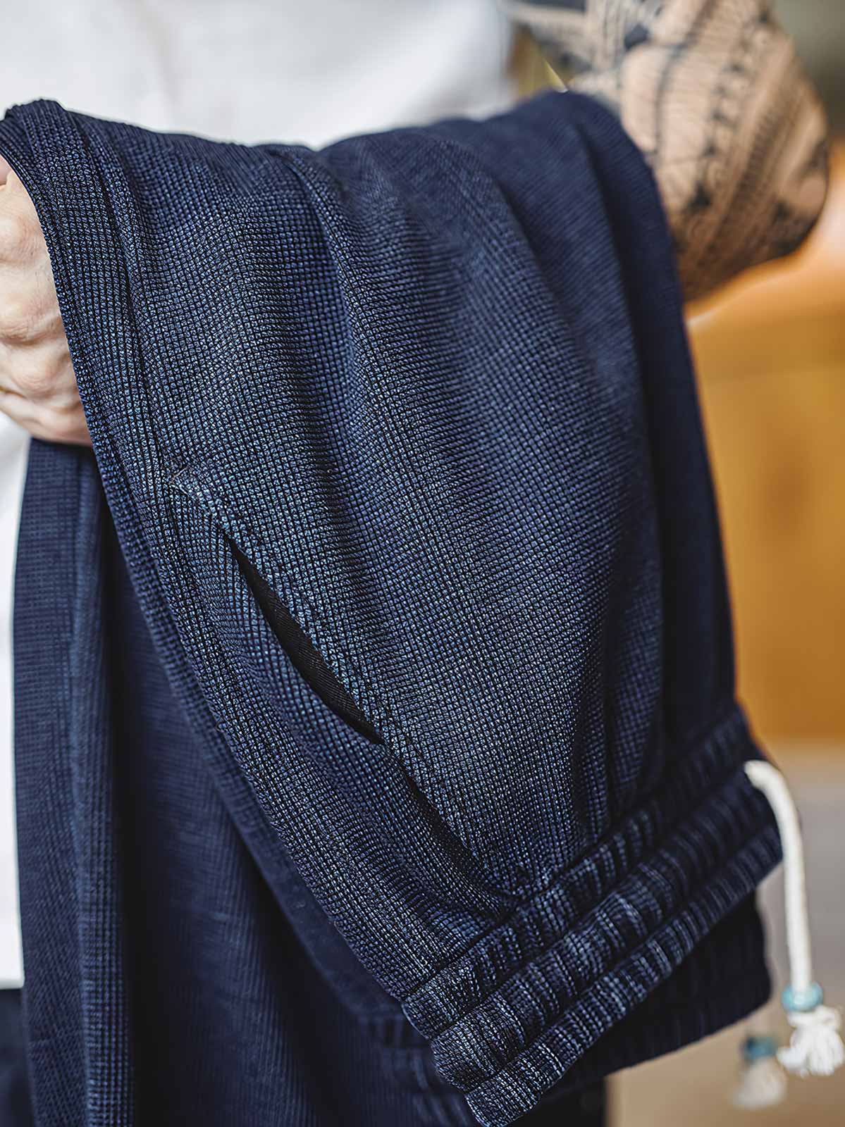 製品画像: ワッフルニットドレープ効果付きカジュアルパンツ正面図
詳細画像: パンツのディテール、白い編み込みドローストリングと石風ビーズ