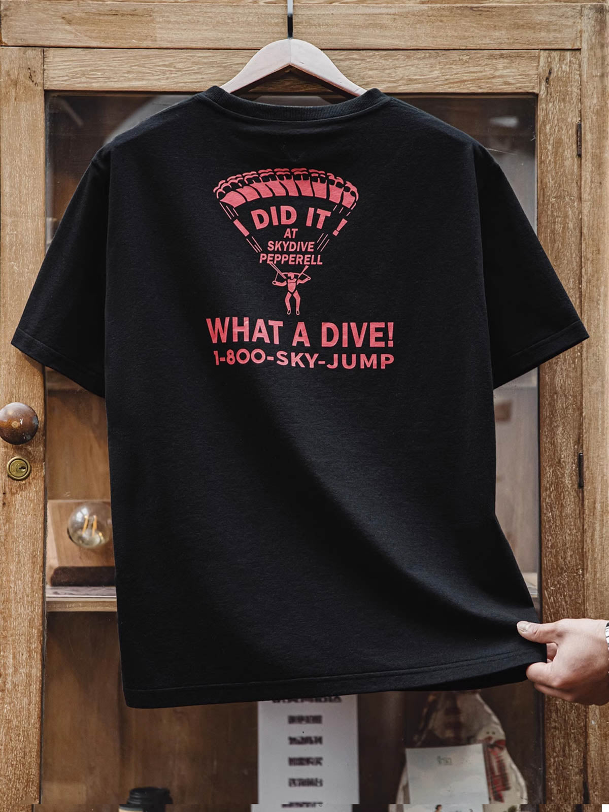 黒の基調に赤いパラシュートパターンレタリングがプリントされた半袖Tシャツ。