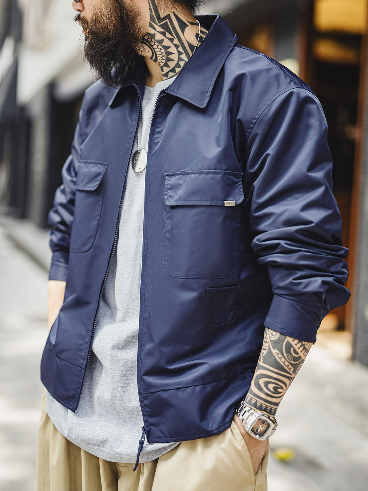 詳細画像
「背面に施された『Hustle is Mentality』スローガンとダイヤモンド型チェーン刺繍のディテール写真。クラシックなデザインと挑戦者の精神を象徴するヴィンテージスタイルのジャケット。」
モデル画像
「モデルがミッドナイトネイビー刺繍ワークジャケットを着用し、防風性のあるコントラストリブ裾やレトロなデザインを活かしたストリートスタイルを披露する写真。」