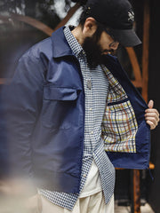 詳細画像
「背面に施された『Hustle is Mentality』スローガンとダイヤモンド型チェーン刺繍のディテール写真。クラシックなデザインと挑戦者の精神を象徴するヴィンテージスタイルのジャケット。」
モデル画像
「モデルがミッドナイトネイビー刺繍ワークジャケットを着用し、防風性のあるコントラストリブ裾やレトロなデザインを活かしたストリートスタイルを披露する写真。」