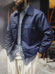 詳細画像
「背面に施された『Hustle is Mentality』スローガンとダイヤモンド型チェーン刺繍のディテール写真。クラシックなデザインと挑戦者の精神を象徴するヴィンテージスタイルのジャケット。」
モデル画像
「モデルがミッドナイトネイビー刺繍ワークジャケットを着用し、防風性のあるコントラストリブ裾やレトロなデザインを活かしたストリートスタイルを披露する写真。」