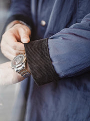 詳細画像:イギリスチェックの裏地と黒のコーデュロイラペルのディテール展示。クラシックなアクセントがコート全体に深いインプレッションをもたらす。
モデル画像:モデルがオーバーサイズのレトロハンティング風コートを着用し、袖口を巻き上げたスタイル。ブーツと合わせてアメリカンワークテイストを演出。