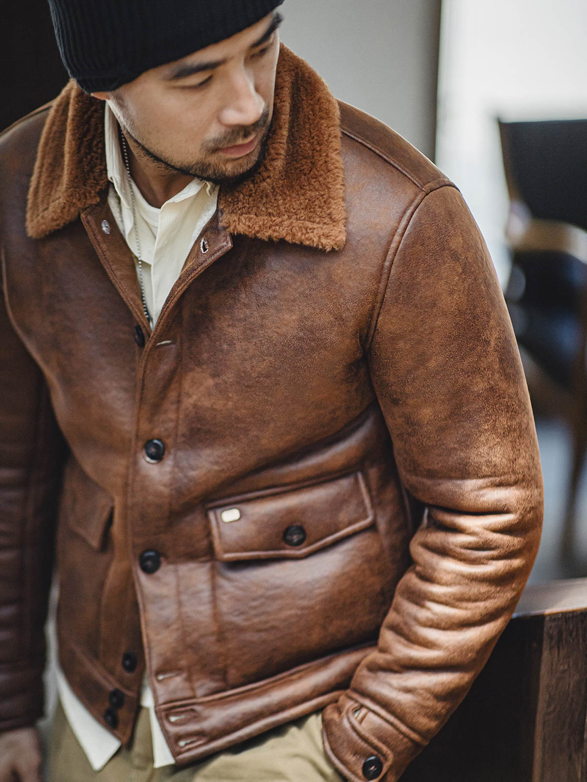 詳細画像:七つボタンの前立てと厚手のシープスキン襟のディテールをクローズアップ。ヴィンテージ感と実用性を兼ね備えた仕様。
モデル画像:モデルがムートンボマージャケットを着用し、デニムパンツとワークブーツを合わせたハードなバイカースタイルを提案。
