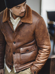 詳細画像:七つボタンの前立てと厚手のシープスキン襟のディテールをクローズアップ。ヴィンテージ感と実用性を兼ね備えた仕様。
モデル画像:モデルがムートンボマージャケットを着用し、デニムパンツとワークブーツを合わせたハードなバイカースタイルを提案。