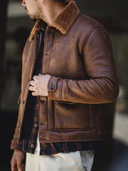 詳細画像:七つボタンの前立てと厚手のシープスキン襟のディテールをクローズアップ。ヴィンテージ感と実用性を兼ね備えた仕様。
モデル画像:モデルがムートンボマージャケットを着用し、デニムパンツとワークブーツを合わせたハードなバイカースタイルを提案。