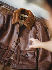 詳細画像:七つボタンの前立てと厚手のシープスキン襟のディテールをクローズアップ。ヴィンテージ感と実用性を兼ね備えた仕様。
モデル画像:モデルがムートンボマージャケットを着用し、デニムパンツとワークブーツを合わせたハードなバイカースタイルを提案。