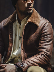 詳細画像:七つボタンの前立てと厚手のシープスキン襟のディテールをクローズアップ。ヴィンテージ感と実用性を兼ね備えた仕様。
モデル画像:モデルがムートンボマージャケットを着用し、デニムパンツとワークブーツを合わせたハードなバイカースタイルを提案。