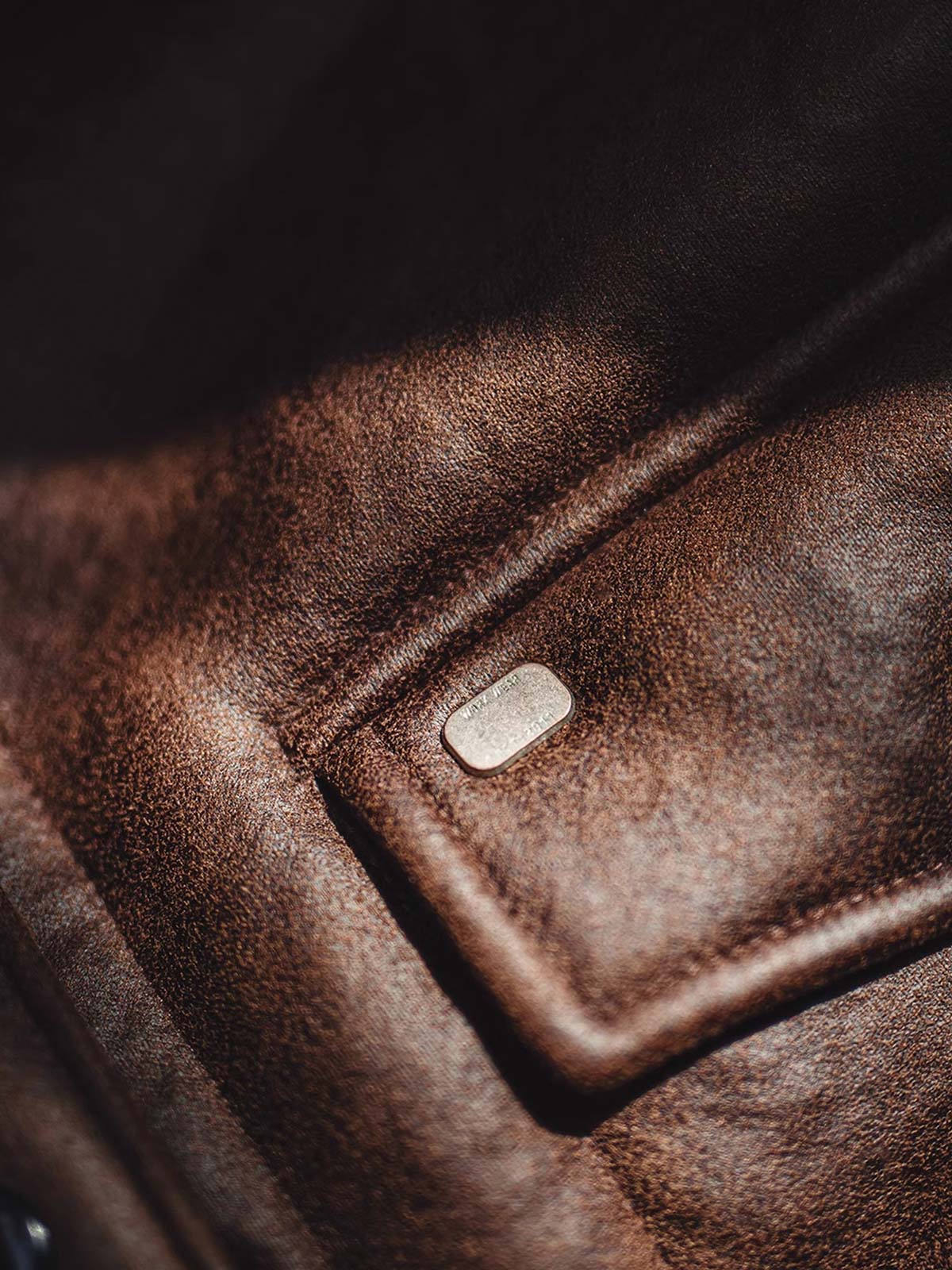 製品画像:アメリカンヴィンテージ風ムートンボマージャケットの正面展示。モカブラウンのレザー表面に色落ち加工が施され、クラシックな雰囲気を演出。
詳細画像:七つボタンの前立てと厚手のシープスキン襟のディテールをクローズアップ。ヴィンテージ感と実用性を兼ね備えた仕様。