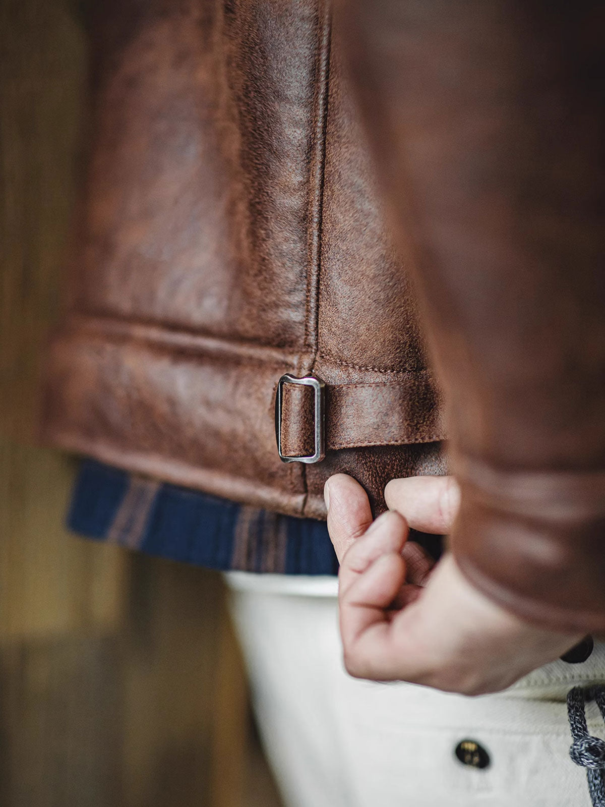 製品画像:アメリカンヴィンテージ風ムートンボマージャケットの正面展示。モカブラウンのレザー表面に色落ち加工が施され、クラシックな雰囲気を演出。
詳細画像:七つボタンの前立てと厚手のシープスキン襟のディテールをクローズアップ。ヴィンテージ感と実用性を兼ね備えた仕様。