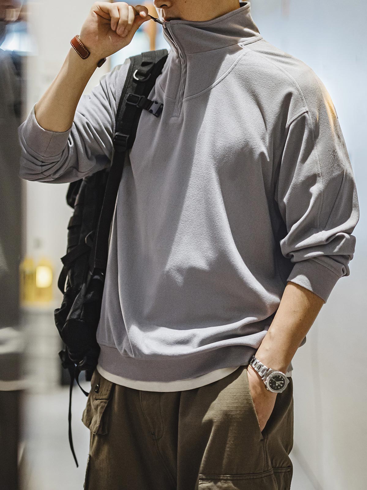 詳細画像: セーターのディテール、ホワイトブラスジッパー、肩と腕のカラー・ブロックデザインが強調されたクローズアップ画像。
モデル画像: モデルがスモーキーグレーのハーフラウンドジップスタンドカラーポロシャツを着用し、カジュアルな秋冬スタイルを演出する画像。