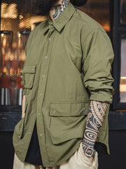 詳細画像
マットな5本爪スナップボタンと、戦地カメラマンの実用性を考慮して配置された3つのフラップ付きポケットのディテール特写。独自のシワ加工が施され、経年変化を楽しめる仕上がり
モデル画像
ノマドジャーナリストシャツを着用したコーディネート例。肩幅にゆとりを持たせたルーズフィットデザインが、ミリタリースタイルと現代的なワークウェアとしての快適さを融合したスタイリングを演出