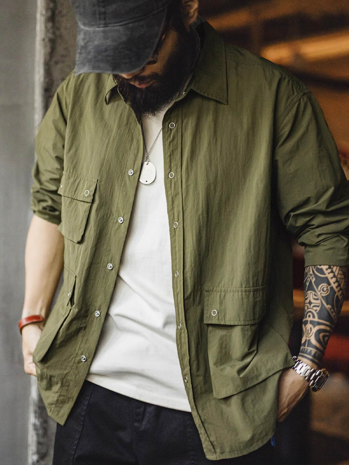 詳細画像
マットな5本爪スナップボタンと、戦地カメラマンの実用性を考慮して配置された3つのフラップ付きポケットのディテール特写。独自のシワ加工が施され、経年変化を楽しめる仕上がり
モデル画像
ノマドジャーナリストシャツを着用したコーディネート例。肩幅にゆとりを持たせたルーズフィットデザインが、ミリタリースタイルと現代的なワークウェアとしての快適さを融合したスタイリングを演出