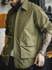 ノマドジャーナリストシャツを着用したコーディネート例。肩幅にゆとりを持たせたルーズフィットデザインが、ミリタリースタイルと現代的なワークウェアとしての快適さを融合したスタイリングを演出