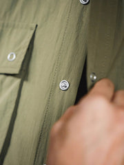 マットな5本爪スナップボタンと、戦地カメラマンの実用性を考慮して配置された3つのフラップ付きポケットのディテール特写。独自のシワ加工が施され、経年変化を楽しめる仕上がり