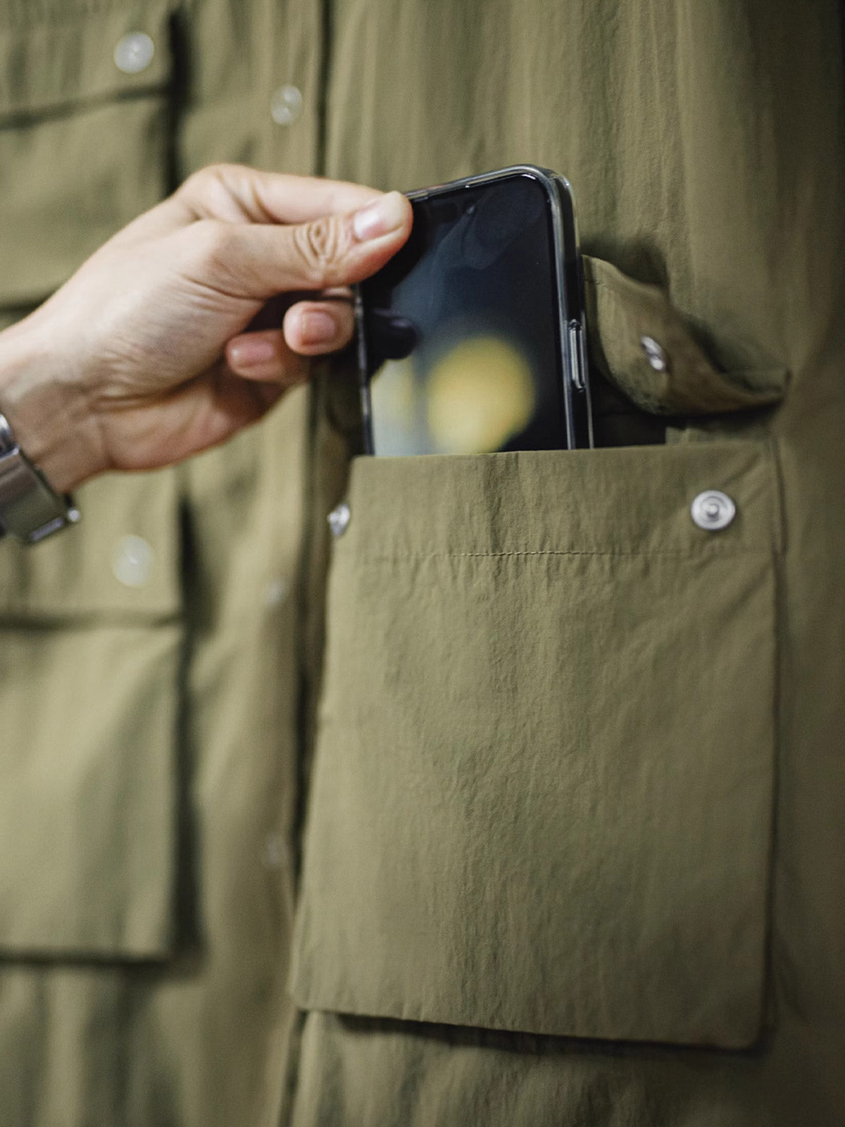 マットな5本爪スナップボタンと、戦地カメラマンの実用性を考慮して配置された3つのフラップ付きポケットのディテール特写。独自のシワ加工が施され、経年変化を楽しめる仕上がり