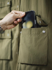 マットな5本爪スナップボタンと、戦地カメラマンの実用性を考慮して配置された3つのフラップ付きポケットのディテール特写。独自のシワ加工が施され、経年変化を楽しめる仕上がり