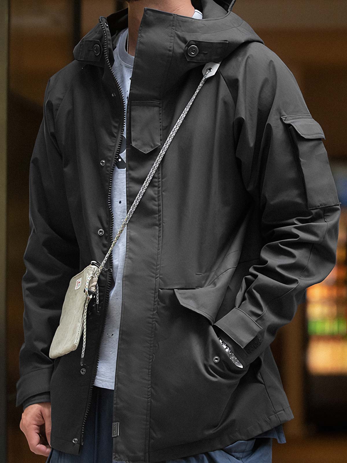 詳細画像: ドローコード付きのフードと左側の機能ポケット、スナップボタンが付いた斜めポケットのディテール。ダブルジップ仕様で実用性を強化
モデル画像: モデルが着用した機能性ナイロンコートの全身スタイリング。秋のデイリースタイルに合わせたルーズフィットで、アウトドアや通勤に適したコート