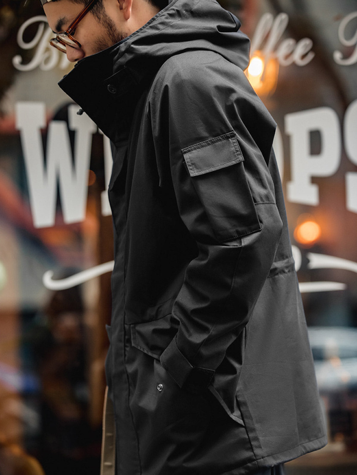 詳細画像: ドローコード付きのフードと左側の機能ポケット、スナップボタンが付いた斜めポケットのディテール。ダブルジップ仕様で実用性を強化
モデル画像: モデルが着用した機能性ナイロンコートの全身スタイリング。秋のデイリースタイルに合わせたルーズフィットで、アウトドアや通勤に適したコート