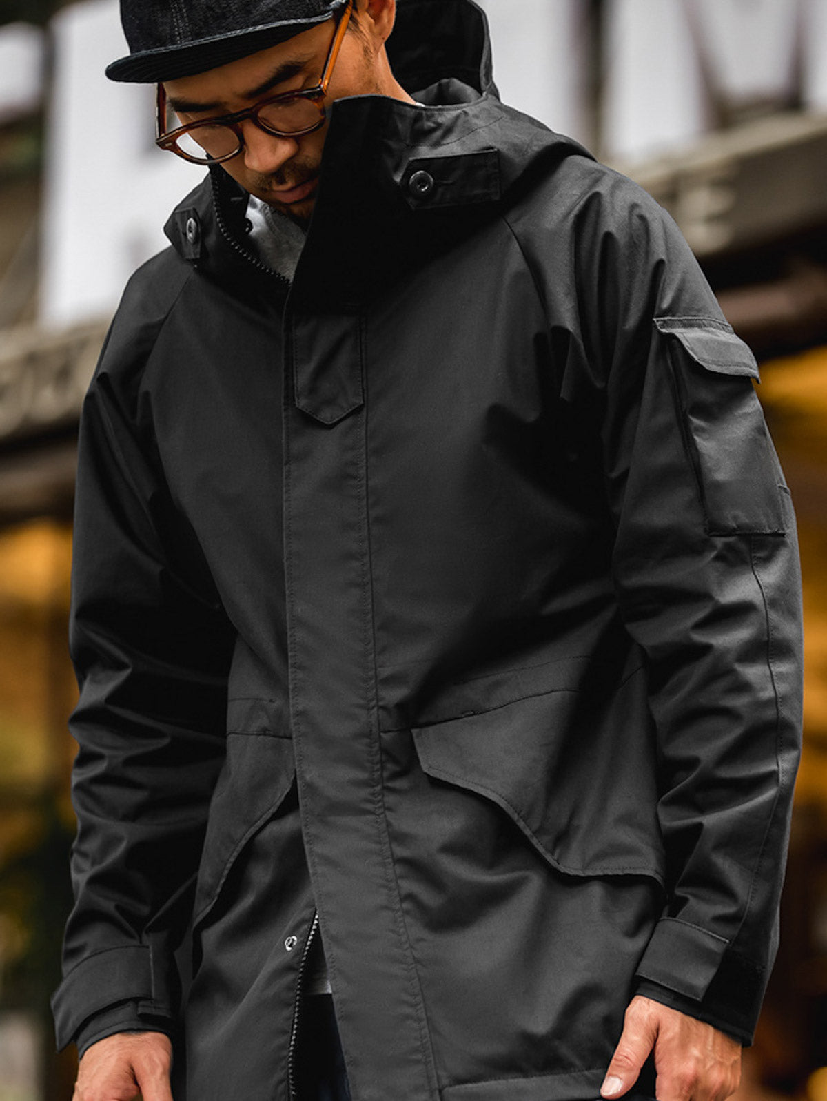 詳細画像: ドローコード付きのフードと左側の機能ポケット、スナップボタンが付いた斜めポケットのディテール。ダブルジップ仕様で実用性を強化
モデル画像: モデルが着用した機能性ナイロンコートの全身スタイリング。秋のデイリースタイルに合わせたルーズフィットで、アウトドアや通勤に適したコート