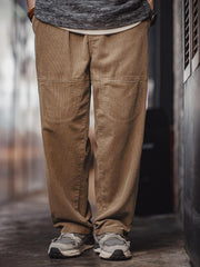 詳細画像: 木目調ボタンや多ポケットデザインのディテール表示。アンティーク風のメタルタグや異なるベルトループの幅がアクセント。
モデル画像: 男性モデルが着用する秋冬ヴィンテージコーデュロイパンツ。ゆったりとしたシルエットと実用的なポケットが魅力のカジュアルスタイル。