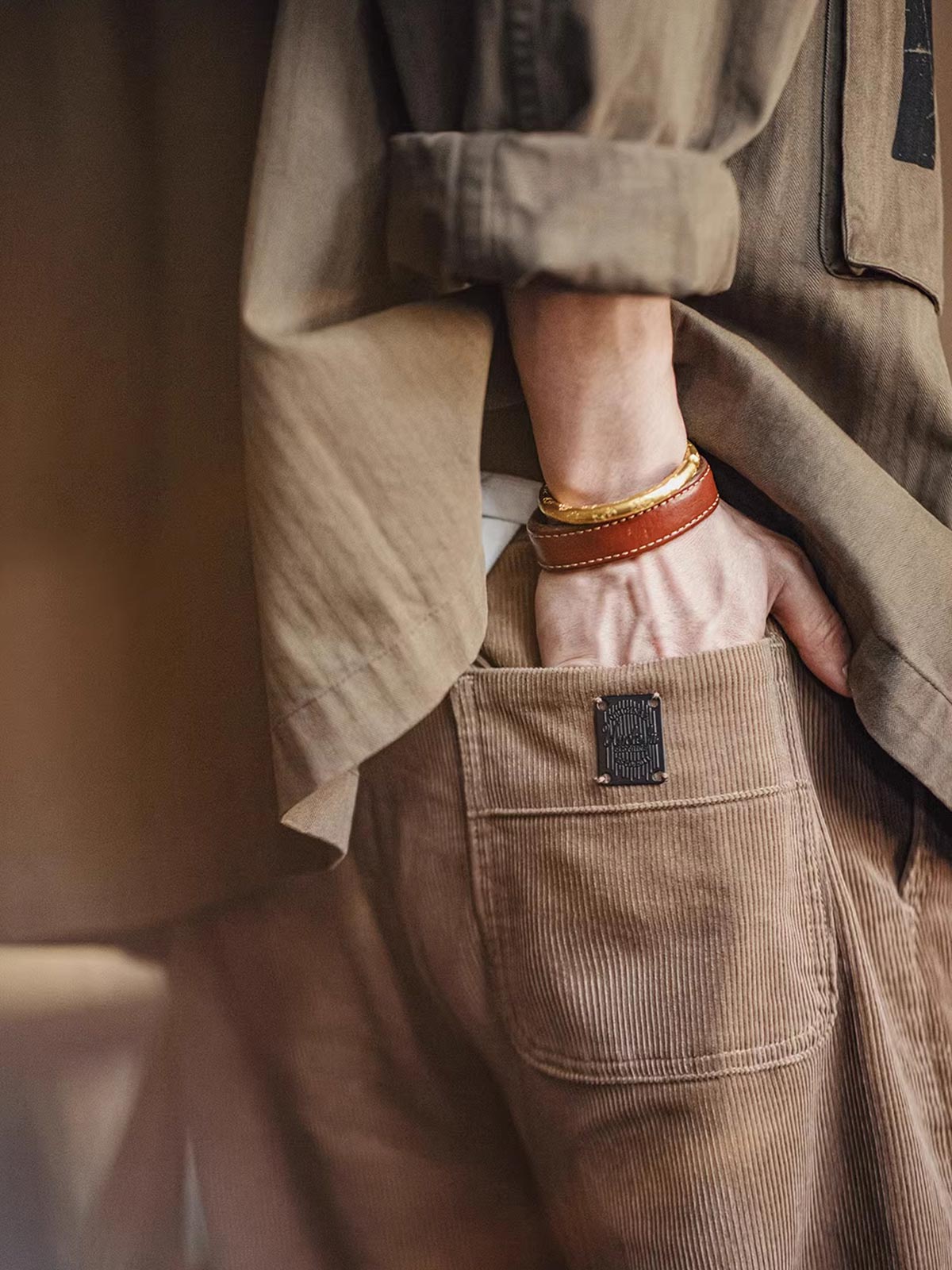 製品画像: ヴィンテージ風多ポケットコーデュロイカジュアルパンツ全体表示。11ウェールコーデュロイとレイヤード感が特徴で、秋冬スタイルに適したデザイン。
詳細画像: 木目調ボタンや多ポケットデザインのディテール表示。アンティーク風のメタルタグや異なるベルトループの幅がアクセント。