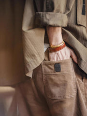製品画像: ヴィンテージ風多ポケットコーデュロイカジュアルパンツ全体表示。11ウェールコーデュロイとレイヤード感が特徴で、秋冬スタイルに適したデザイン。
詳細画像: 木目調ボタンや多ポケットデザインのディテール表示。アンティーク風のメタルタグや異なるベルトループの幅がアクセント。