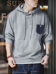 詳細画像:
「霜降り模様のコットン感ストレッチニット生地と、白いステッチと刻印入り銅製ボタンをあしらったデニムポケットのディテールクローズアップ。パッチワークデザインがヴィンテージ感と立体感を強調。」
モデル画像:
「モデルがデニムポケット付き パッチワーク パーカーを着用し、スポーティーなヴィンテージスタイルを披露。ゆったりとしたルーズフィットのシルエットが、カジュアルシーンからスポーツスタイルまで幅広く対応。」