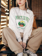 モデルがPESSOA CLUBのグレーのキャンプテーマ刺繍スウェットシャツを着用し、都会的なカジュアルスタイルを披露