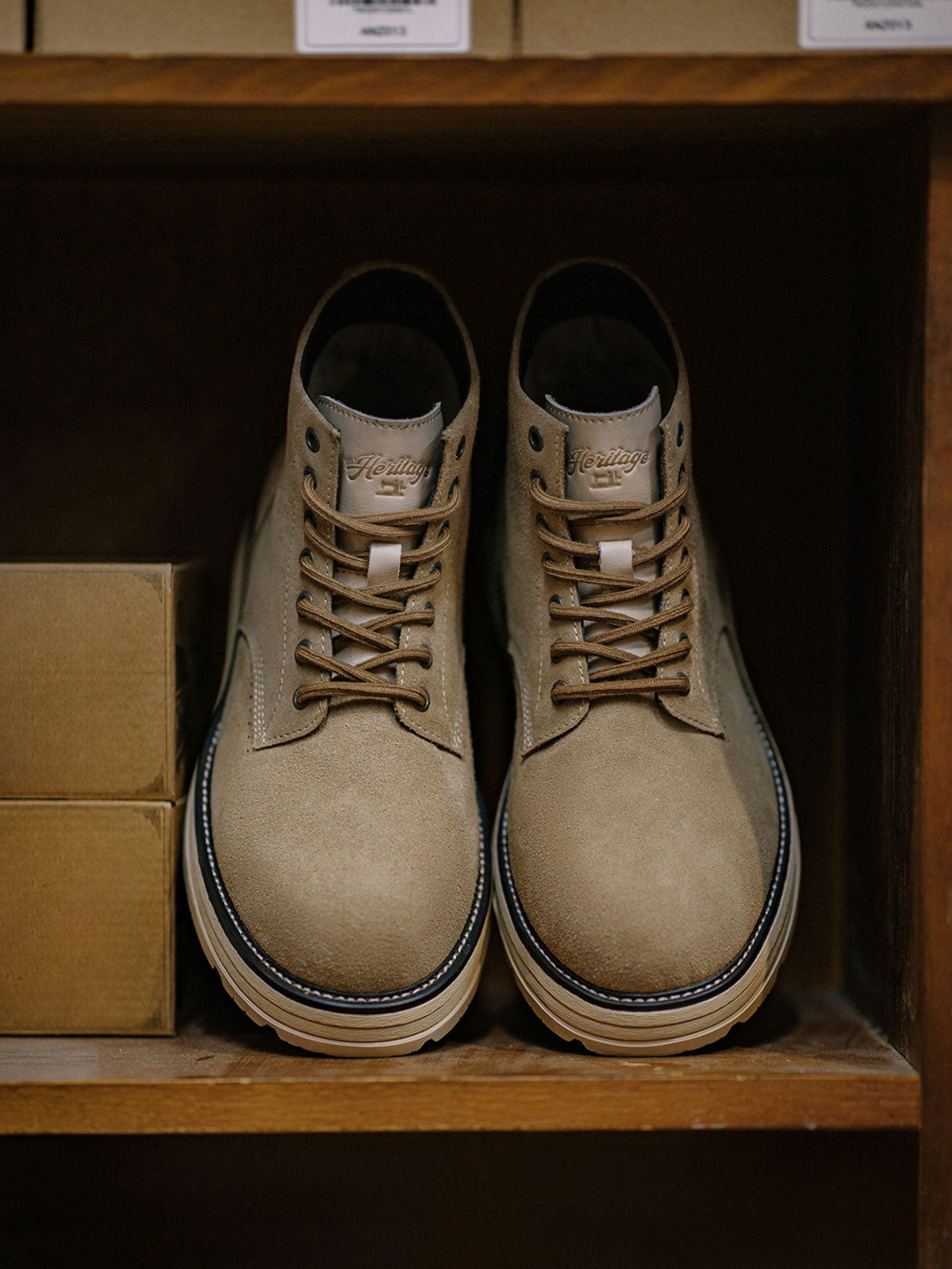 製品画像: 厳選された牛革スエードと特注厚底デザインを組み合わせたヴィンテージ感漂うワークブーツ全体像、グラベルカラーのトーンが特徴。
詳細画像: 牛革スエードのアッパー、PUレザー靴舌、白いステッチが際立つラバーディテールのクローズアップ。