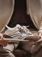 製品画像: 60Sピースバスケットシューズ正面展示画像。長毛感のあるスエード革と異素材のコンビネーションが特徴で、ネイビーブルーのエレクトリック刺繍矢印ロゴがサイドに配置されています。ヒール部分にはブラックの本革と金色のレトロな金属刻印が施され、独自のデザインを際立たせています。
詳細画像: 60Sピースバスケットシューズのアッパー部分、長毛感のあるスエード革と異素材のコンビネーションが美しく融合し、レトロ感を強調しています。金色のレトロ金属刻印と刺繍のディテールがシューズに高級感を与えています。