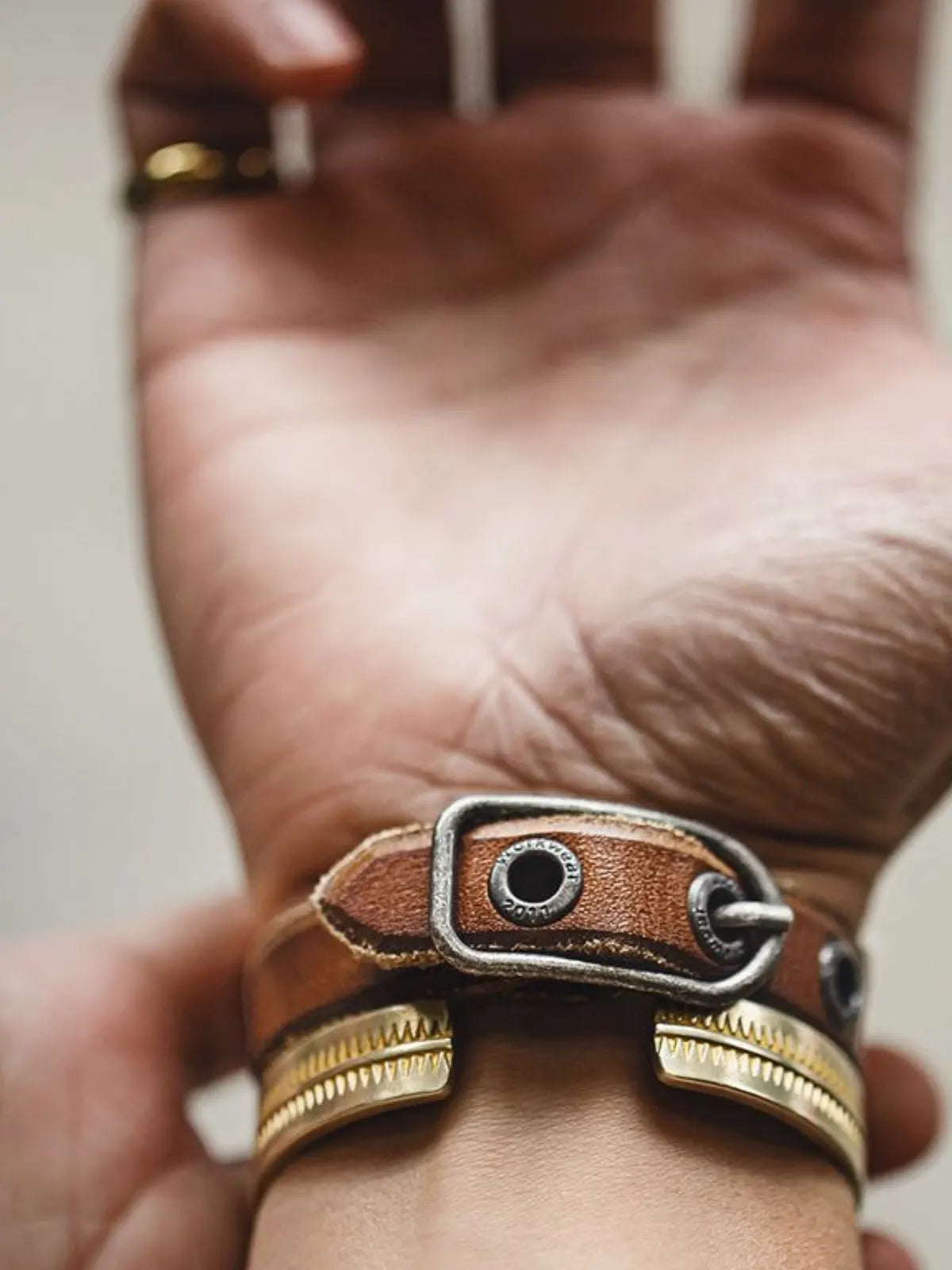 茶色のレザーブレスレット、幅広のベルトとヴィンテージ加工されたバックルが特徴的