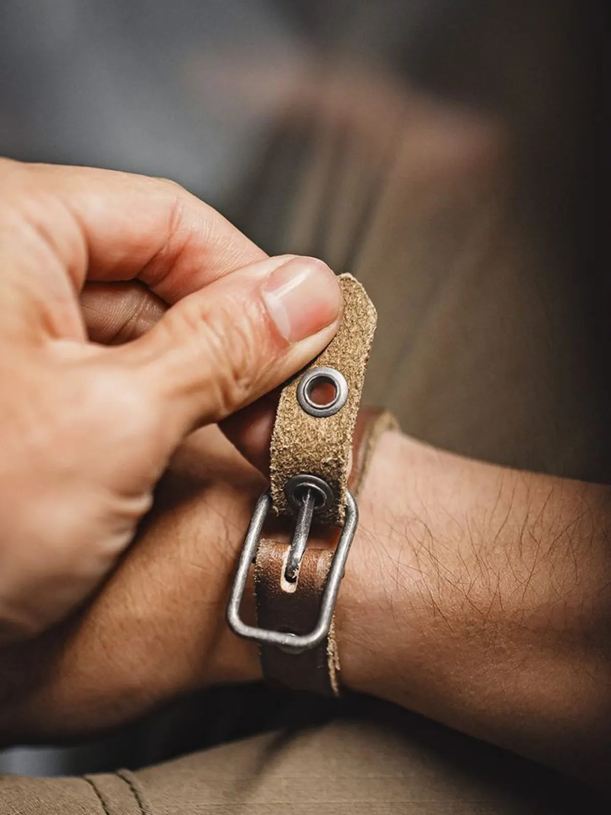 茶色のレザーブレスレット、幅広のベルトとヴィンテージ加工されたバックルが特徴的