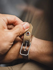 茶色のレザーブレスレット、幅広のベルトとヴィンテージ加工されたバックルが特徴的