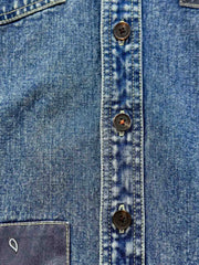 デニムシャツの袖口にあるタイスリーブノットとポケットのステッチラインのクローズアップ。手作業の細かなデテールが強調されている。