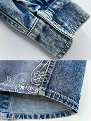 デニムシャツの袖口にあるタイスリーブノットとポケットのステッチラインのクローズアップ。手作業の細かなデテールが強調されている。