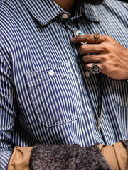 詳細画像: 1930年代の鉄道文化からインスパイアされたストライプデザインのディテール。ダブル胸ポケットとクラシックな開襟が特徴的で、100%コットン素材の快適な着心地。
モデル画像: モデルがレールストライプ長袖シャツを着用し、アメリカンレトロなスタイルで作業服パンツやデニムとのコーディネートを披露。春秋のレイヤードスタイルにも最適なゆったりフィット。