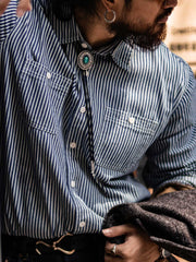 詳細画像: 1930年代の鉄道文化からインスパイアされたストライプデザインのディテール。ダブル胸ポケットとクラシックな開襟が特徴的で、100%コットン素材の快適な着心地。
モデル画像: モデルがレールストライプ長袖シャツを着用し、アメリカンレトロなスタイルで作業服パンツやデニムとのコーディネートを披露。春秋のレイヤードスタイルにも最適なゆったりフィット。