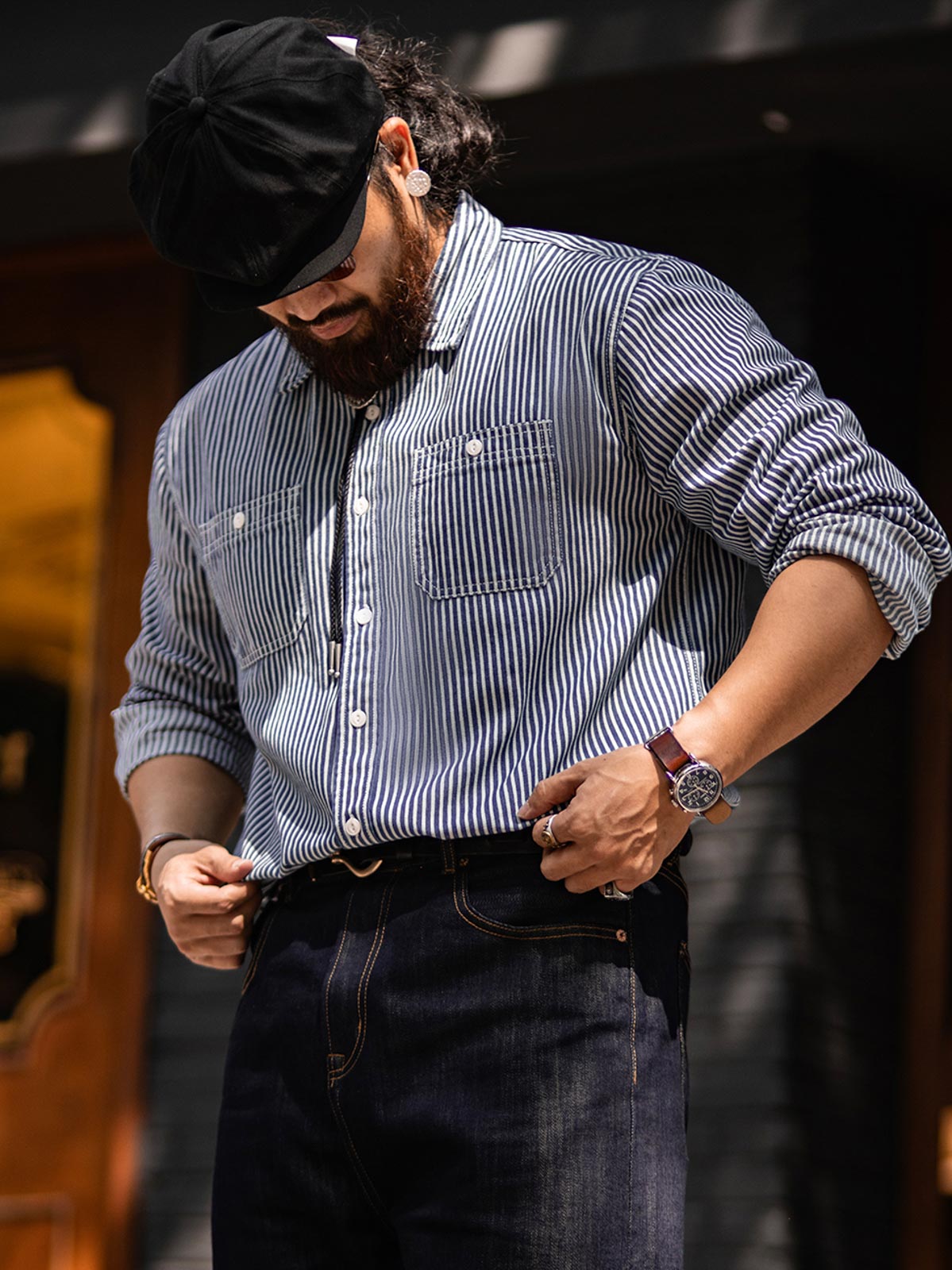 詳細画像: 1930年代の鉄道文化からインスパイアされたストライプデザインのディテール。ダブル胸ポケットとクラシックな開襟が特徴的で、100%コットン素材の快適な着心地。
モデル画像: モデルがレールストライプ長袖シャツを着用し、アメリカンレトロなスタイルで作業服パンツやデニムとのコーディネートを披露。春秋のレイヤードスタイルにも最適なゆったりフィット。