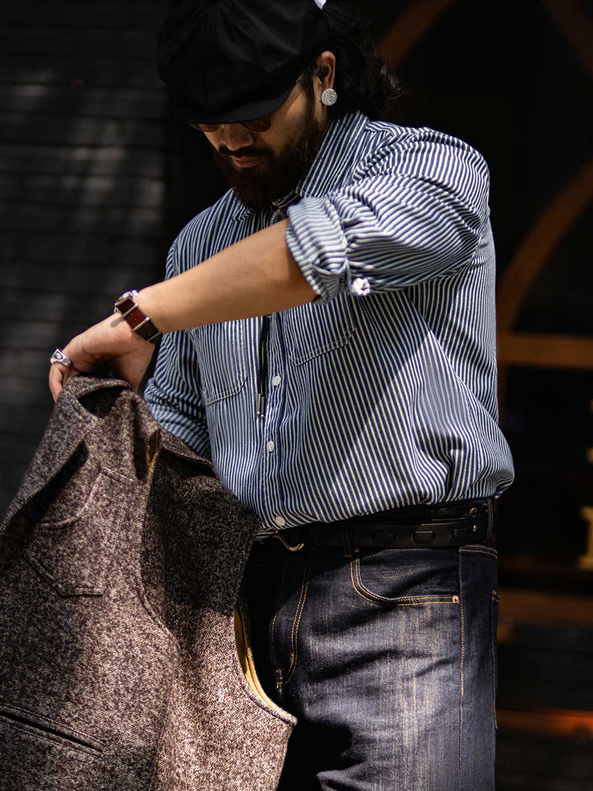 詳細画像: 1930年代の鉄道文化からインスパイアされたストライプデザインのディテール。ダブル胸ポケットとクラシックな開襟が特徴的で、100%コットン素材の快適な着心地。
モデル画像: モデルがレールストライプ長袖シャツを着用し、アメリカンレトロなスタイルで作業服パンツやデニムとのコーディネートを披露。春秋のレイヤードスタイルにも最適なゆったりフィット。