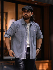 詳細画像: 1930年代の鉄道文化からインスパイアされたストライプデザインのディテール。ダブル胸ポケットとクラシックな開襟が特徴的で、100%コットン素材の快適な着心地。
モデル画像: モデルがレールストライプ長袖シャツを着用し、アメリカンレトロなスタイルで作業服パンツやデニムとのコーディネートを披露。春秋のレイヤードスタイルにも最適なゆったりフィット。