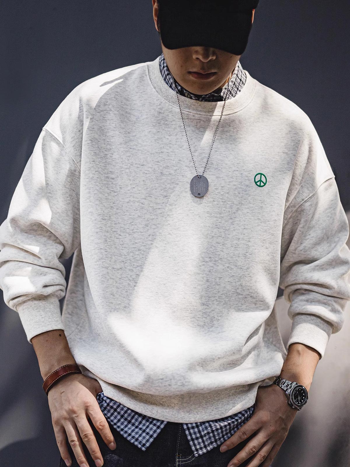 詳細画像: 胸元に配置された精巧な「ピースマーク」プリントとクラシックなリブ仕様のネックや裾をクローズアップした画像。保温性と耐久性を兼ね備えた裏起毛素材が際立つ。
モデル画像: 裏起毛クルーネックスウェットを着用したモデルが、スニーカーとブラックパンツを合わせたカジュアルな秋冬スタイルを提案。快適さと個性を両立したコーディネートが魅力的。