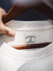 製品画像: ライトグレーの裏起毛クルーネックスウェット全体イメージ画像。リラックスシルエットとドロップショルダーデザインが特徴で、胸元には「ピースマーク」プリントがアクセント。単独でもインナーとしても活躍する秋冬の万能アイテム。
詳細画像: 胸元に配置された精巧な「ピースマーク」プリントとクラシックなリブ仕様のネックや裾をクローズアップした画像。保温性と耐久性を兼ね備えた裏起毛素材が際立つ。