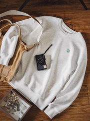 製品画像: ライトグレーの裏起毛クルーネックスウェット全体イメージ画像。リラックスシルエットとドロップショルダーデザインが特徴で、胸元には「ピースマーク」プリントがアクセント。単独でもインナーとしても活躍する秋冬の万能アイテム。
詳細画像: 胸元に配置された精巧な「ピースマーク」プリントとクラシックなリブ仕様のネックや裾をクローズアップした画像。保温性と耐久性を兼ね備えた裏起毛素材が際立つ。