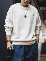 詳細画像: 胸元に配置された精巧な「ピースマーク」プリントとクラシックなリブ仕様のネックや裾をクローズアップした画像。保温性と耐久性を兼ね備えた裏起毛素材が際立つ。
モデル画像: 裏起毛クルーネックスウェットを着用したモデルが、スニーカーとブラックパンツを合わせたカジュアルな秋冬スタイルを提案。快適さと個性を両立したコーディネートが魅力的。