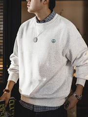 詳細画像: 胸元に配置された精巧な「ピースマーク」プリントとクラシックなリブ仕様のネックや裾をクローズアップした画像。保温性と耐久性を兼ね備えた裏起毛素材が際立つ。
モデル画像: 裏起毛クルーネックスウェットを着用したモデルが、スニーカーとブラックパンツを合わせたカジュアルな秋冬スタイルを提案。快適さと個性を両立したコーディネートが魅力的。